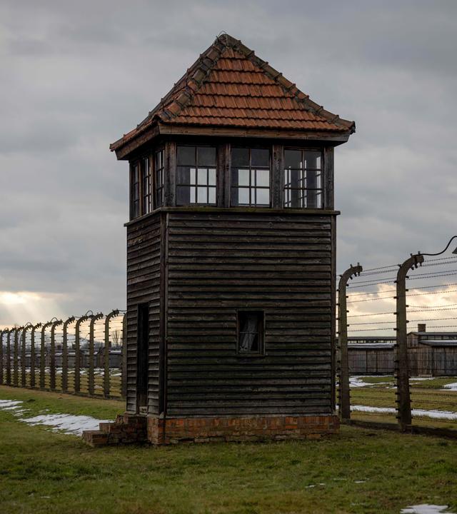 Der Stacheldraht-Zaun vor dem Konzetrationslager Auschwitz mit einem Wachturm.