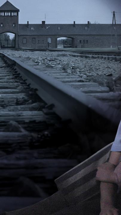 Im Vordergrund zwei Insassen des KZ, ein Liebespaar. Im Hintergrund das KZ Auschwitz