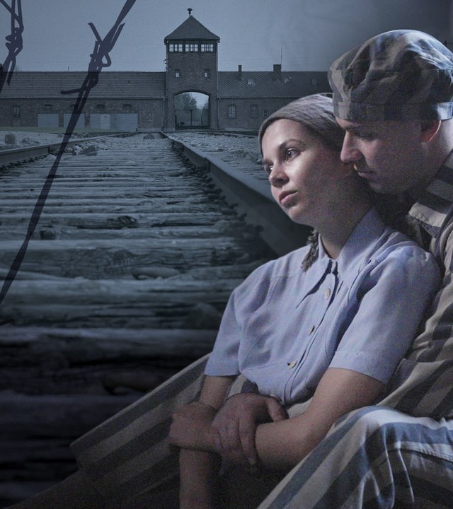 Im Vordergrund zwei Insassen des KZ, ein Liebespaar. Im Hintergrund das KZ Auschwitz