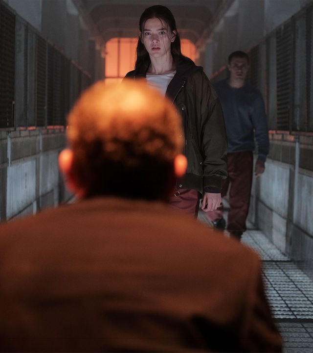 "Fallen - Ausgeflogen": Luce (Jessica Alexander) steht dem Outcast (Rod Hill) mit ernstem Blick gegenüber. Hinter ihr steht Daniel (Gijs Blom) in einem düsteren Gang mit Gitterwänden zu beiden Seiten.