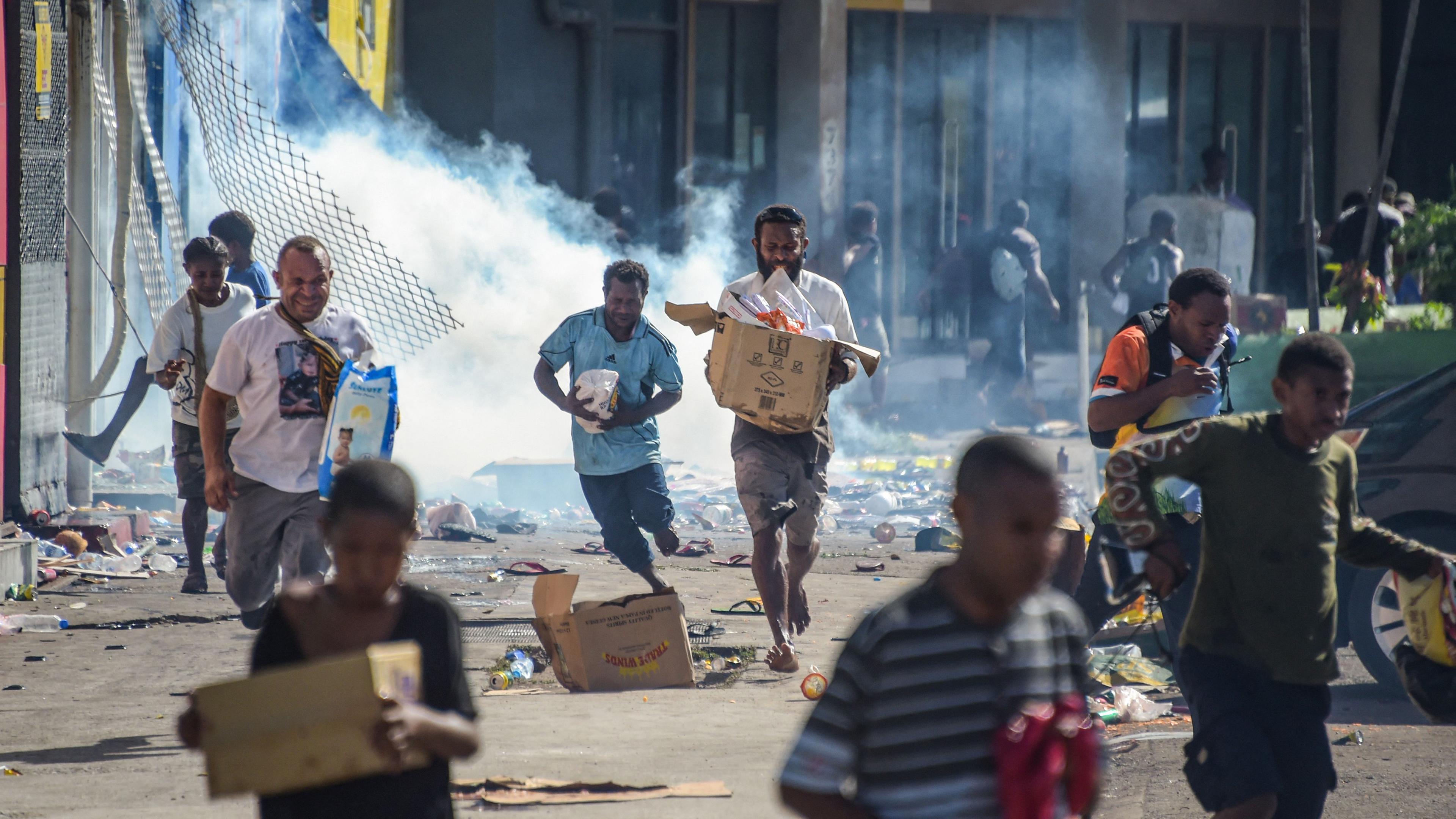 Menschen rennen mit Waren umher, während Menschenmengen in Port Moresby am 10.01.2024 Geschäfte mit geplünderten Waren verlassen.