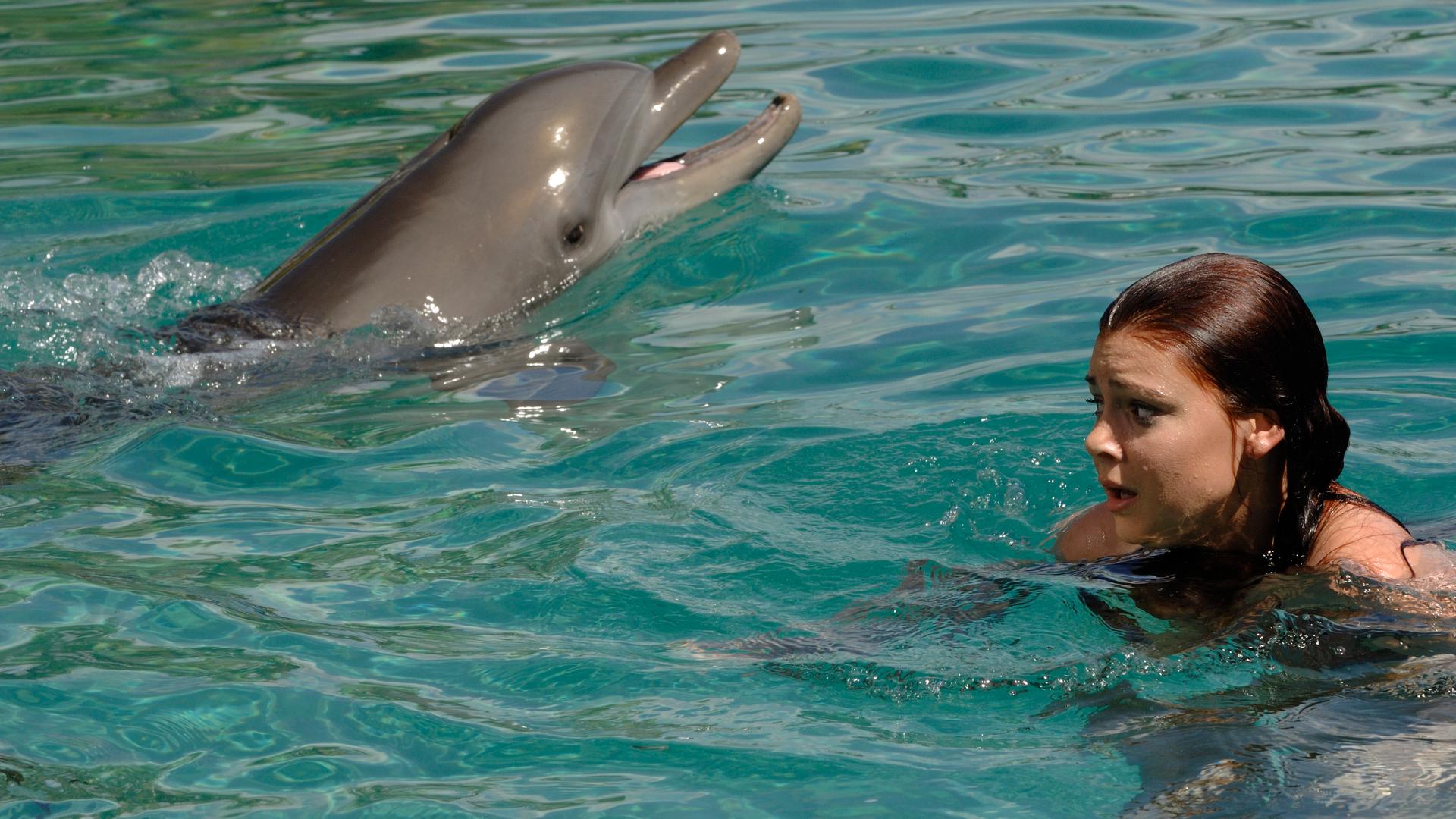 Charlotte hat Angst vor Delfinen. Sie schwimmt mit einem Delfin zusammen an der Wasseroberfläche und sieht sehr ängstlich aus.