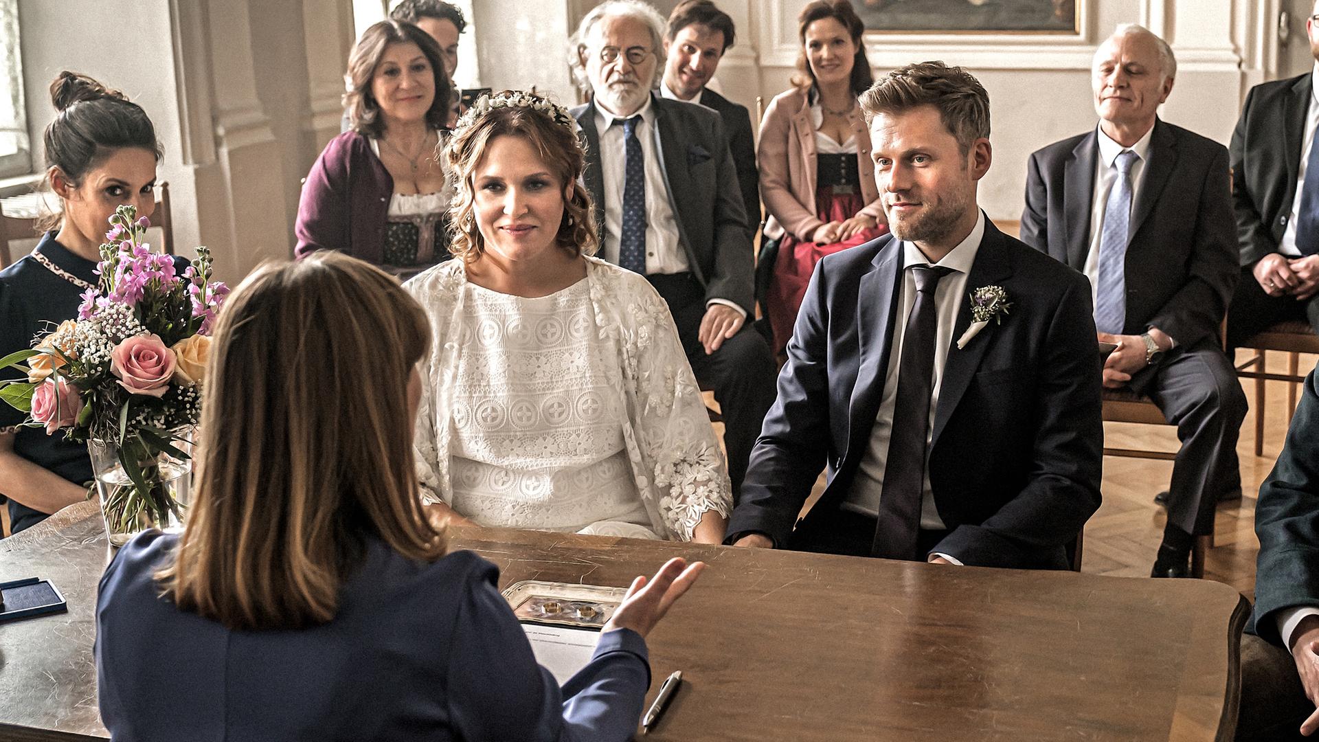  Das Brautpaar Lena Lorenz (Judith Hoersch) und Quirin Pankofer (Jens Atzorn) sitzen an einem antiken Holztisch.