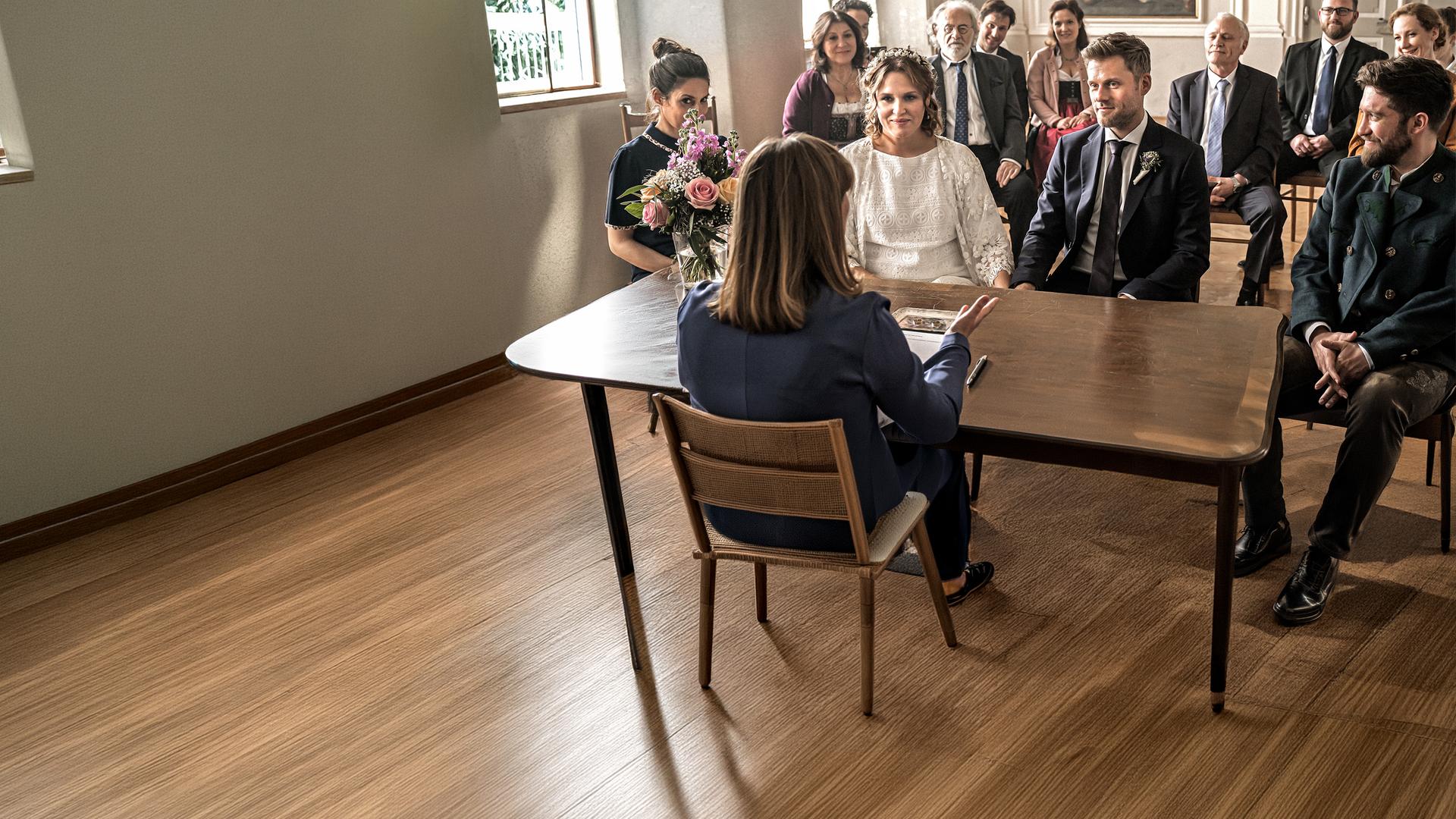  Das Brautpaar Lena Lorenz (Judith Hoersch) und Quirin Pankofer (Jens Atzorn) sitzen an einem antiken Holztisch.