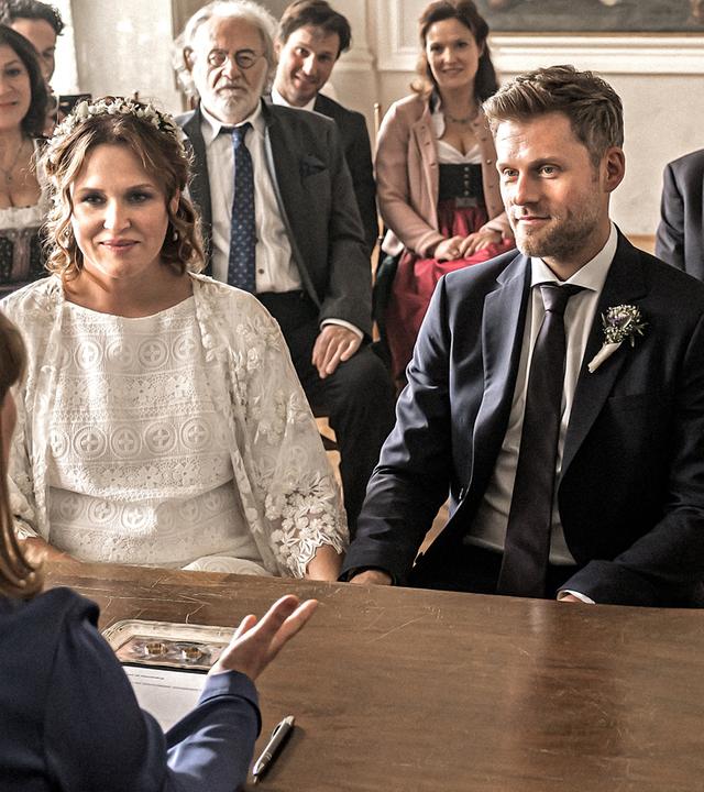  Das Brautpaar Lena Lorenz (Judith Hoersch) und Quirin Pankofer (Jens Atzorn) sitzen an einem antiken Holztisch.