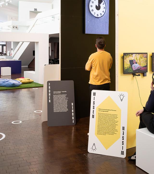 In einem Ausstellungsraum schauen Menschen sich die Exponate an.