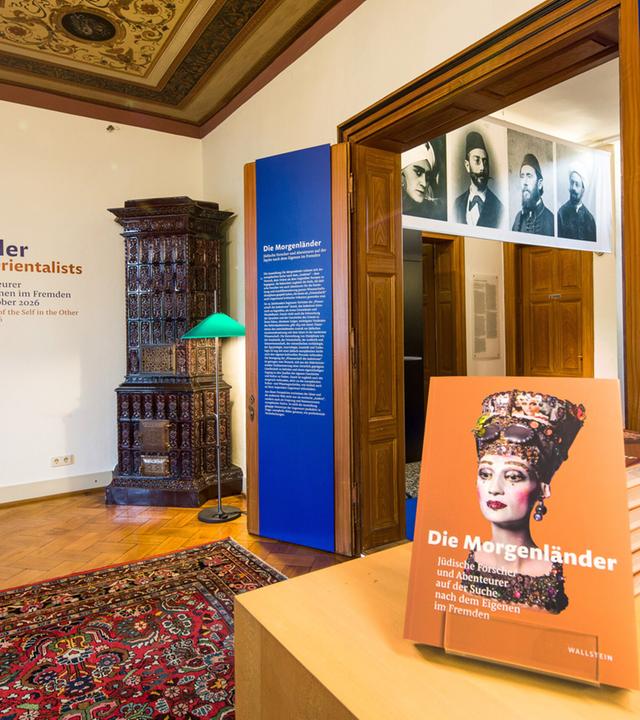 In einem Ausstellungsraum stehen Exponate und hängen Bilder von Personen an der Wand.