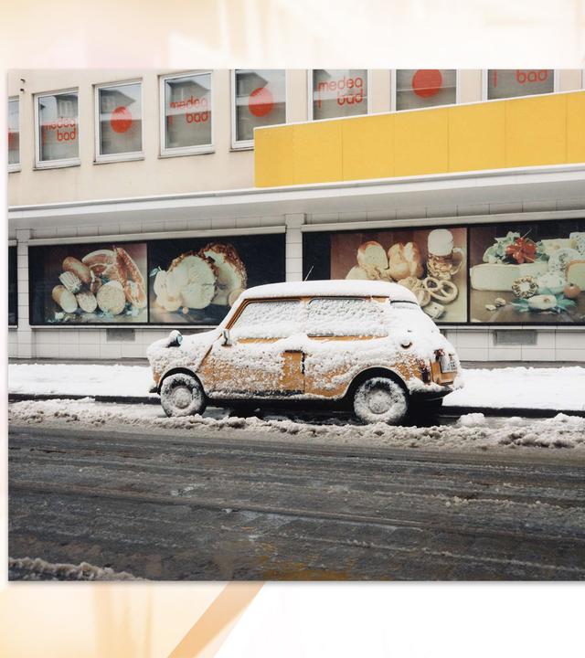 Ein verschneites Auto ist vor einem Geschäft geparkt.