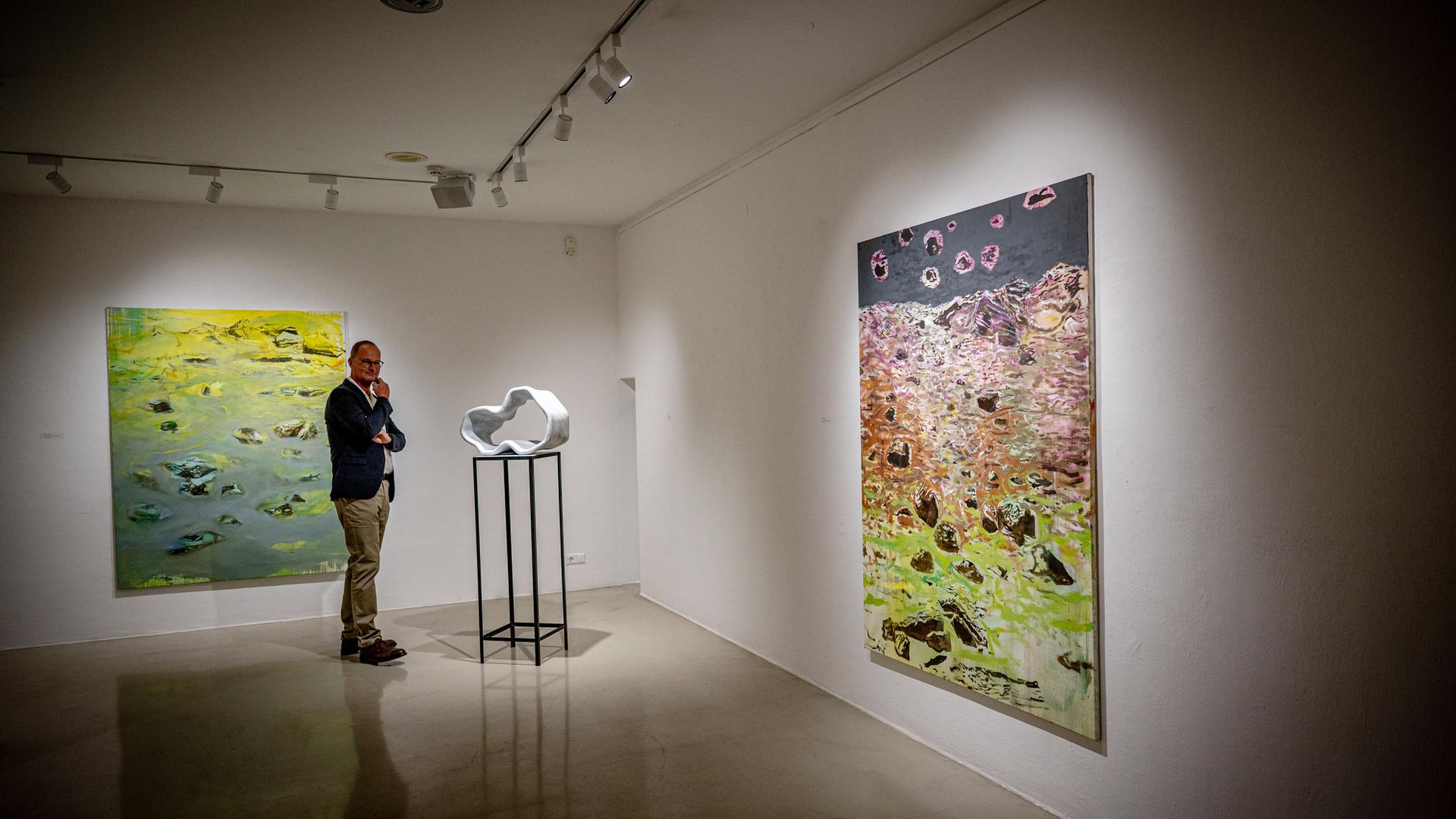 Ein Mann sieht sich eine moderne Skulptur in einem Ausstellungsraum an. An den Wänden hängen abstrakte Gemälde.