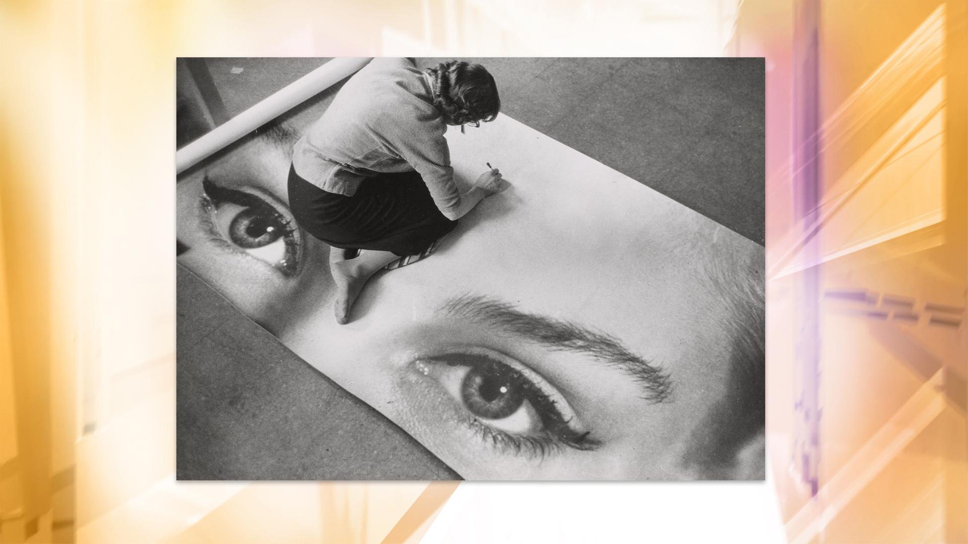 Man sieht eine Schwarz-Weiß-Fotografie, auf der eine Frau am Boden sitzt und an einem Kunstwerk arbeitet.