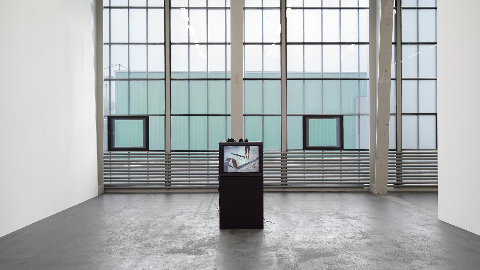 In einem Ausstellungsraum mit großen Fenstern steht eine Videoinstallation.