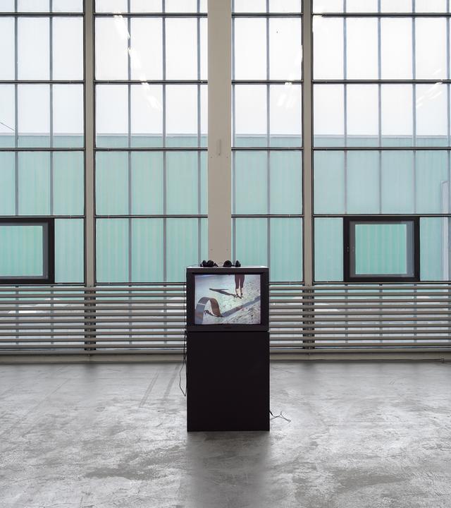 In einem Ausstellungsraum mit großen Fenstern steht eine Videoinstallation.