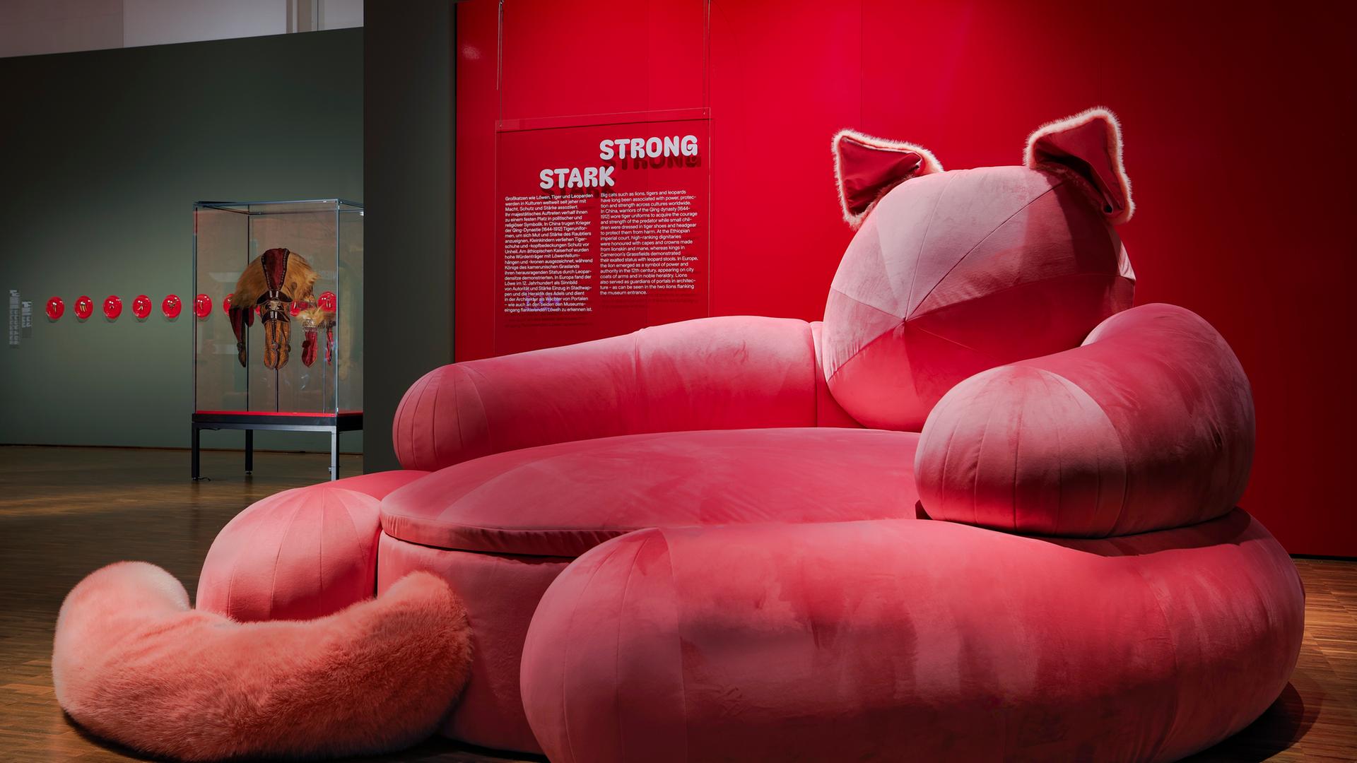 In einem Ausstellungsraum sieht man ein pinkfarbenes Sofa in Form einer Katze.