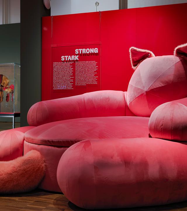In einem Ausstellungsraum sieht man ein pinkfarbenes Sofa in Form einer Katze.