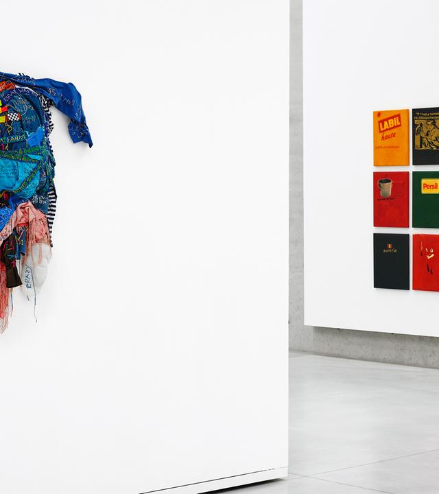 In einem Ausstellungsraum sieht man bunte Kunstwerke an den Wänden.
