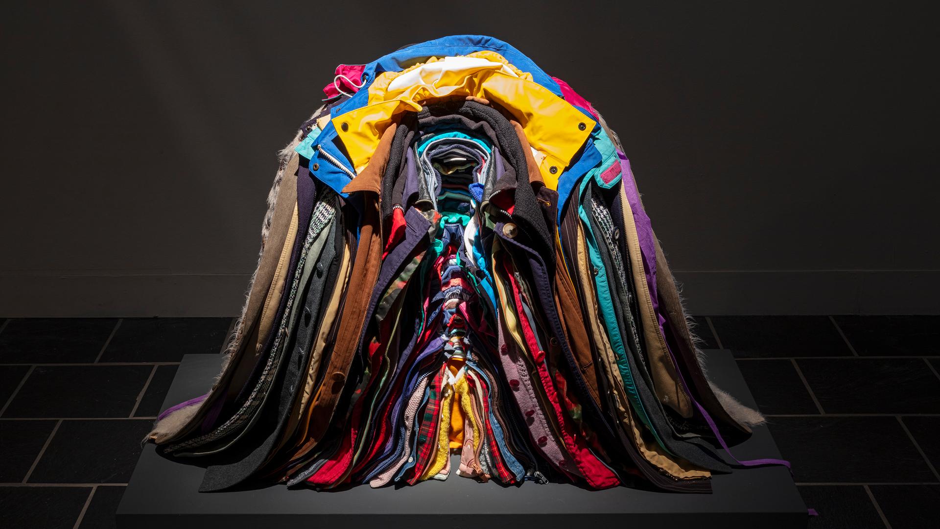 Zu sehen ist ein bunter, ordentlich ineinander gestapelter Haufen aus Jacken.