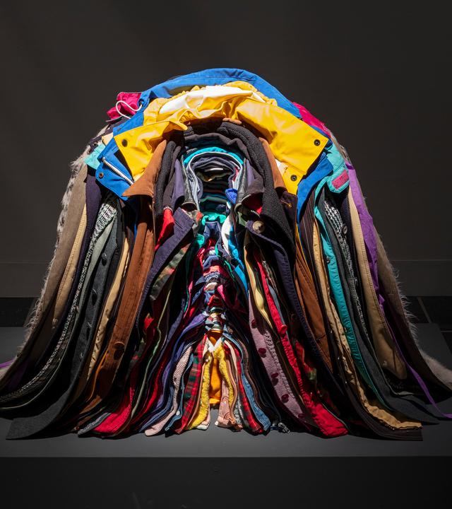 Zu sehen ist ein bunter, ordentlich ineinander gestapelter Haufen aus Jacken.