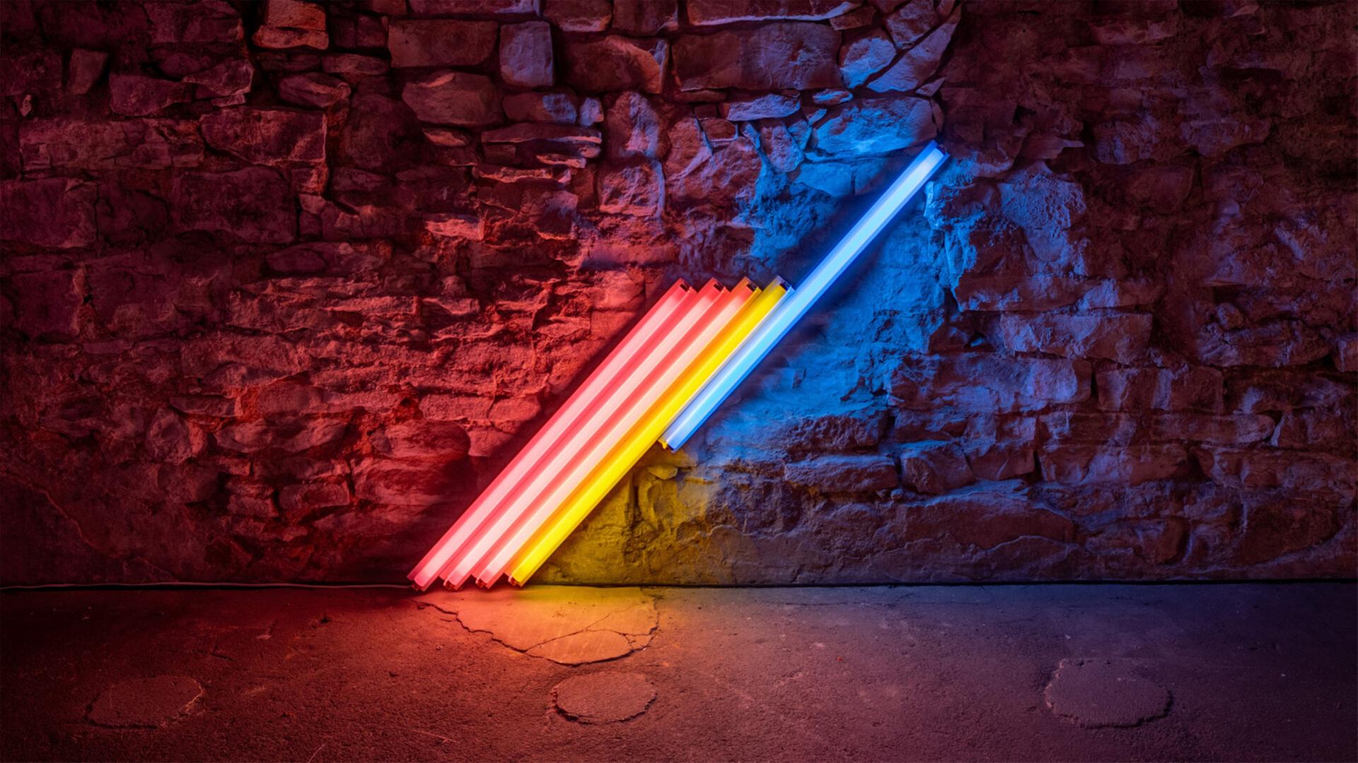 In einem abgedunkelten Ausstellungsraum sieht man eine Installation aus bunten, schräg nebeneinander angeordneten Neonröhren.