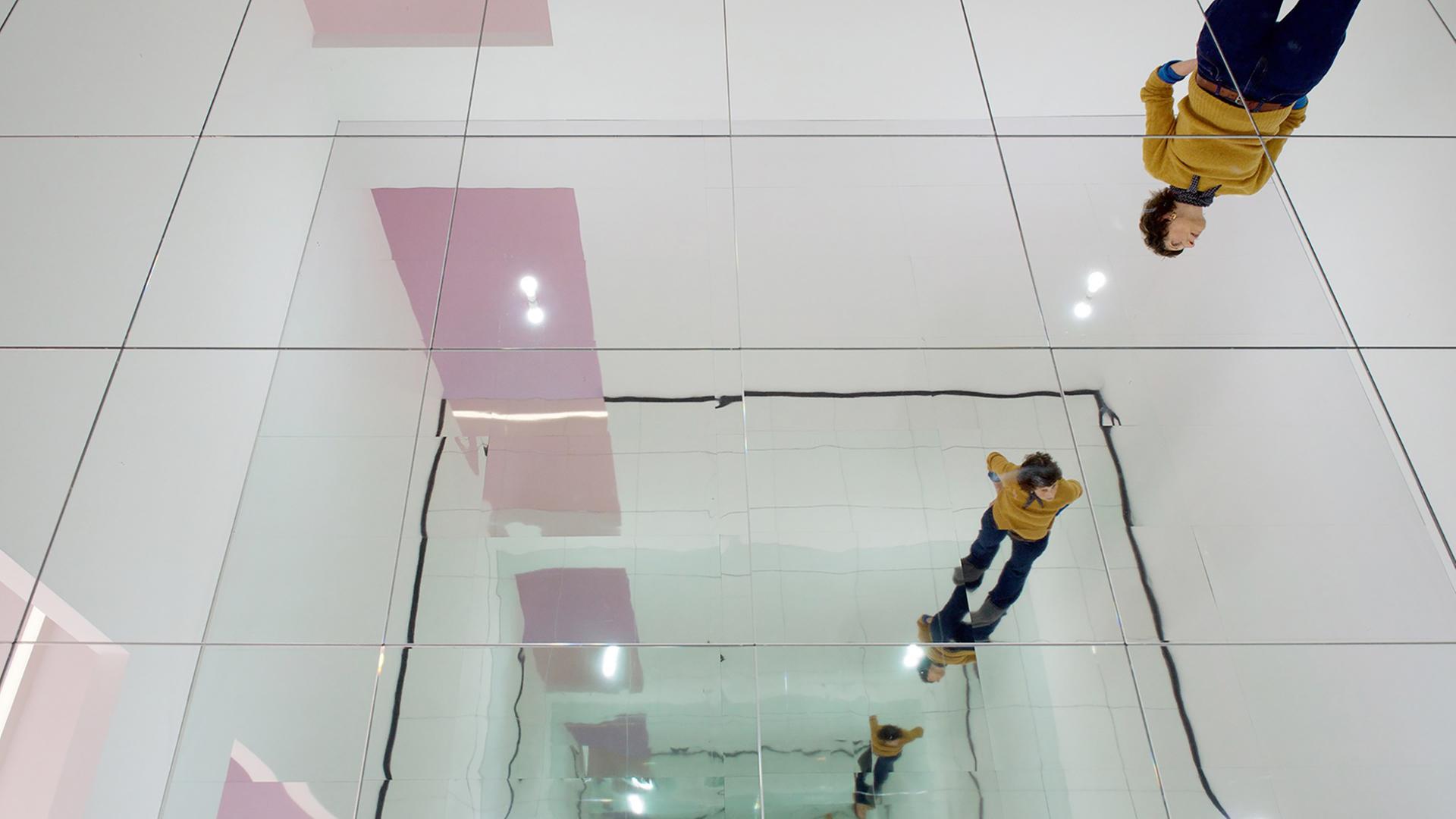 In einem Ausstellungsraum spiegelt sich eine Frau in einer Spiegel-Installation, die eine unendliche Reihe Spiegelbilder erzeugt.