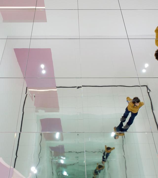 In einem Ausstellungsraum spiegelt sich eine Frau in einer Spiegel-Installation, die eine unendliche Reihe Spiegelbilder erzeugt.
