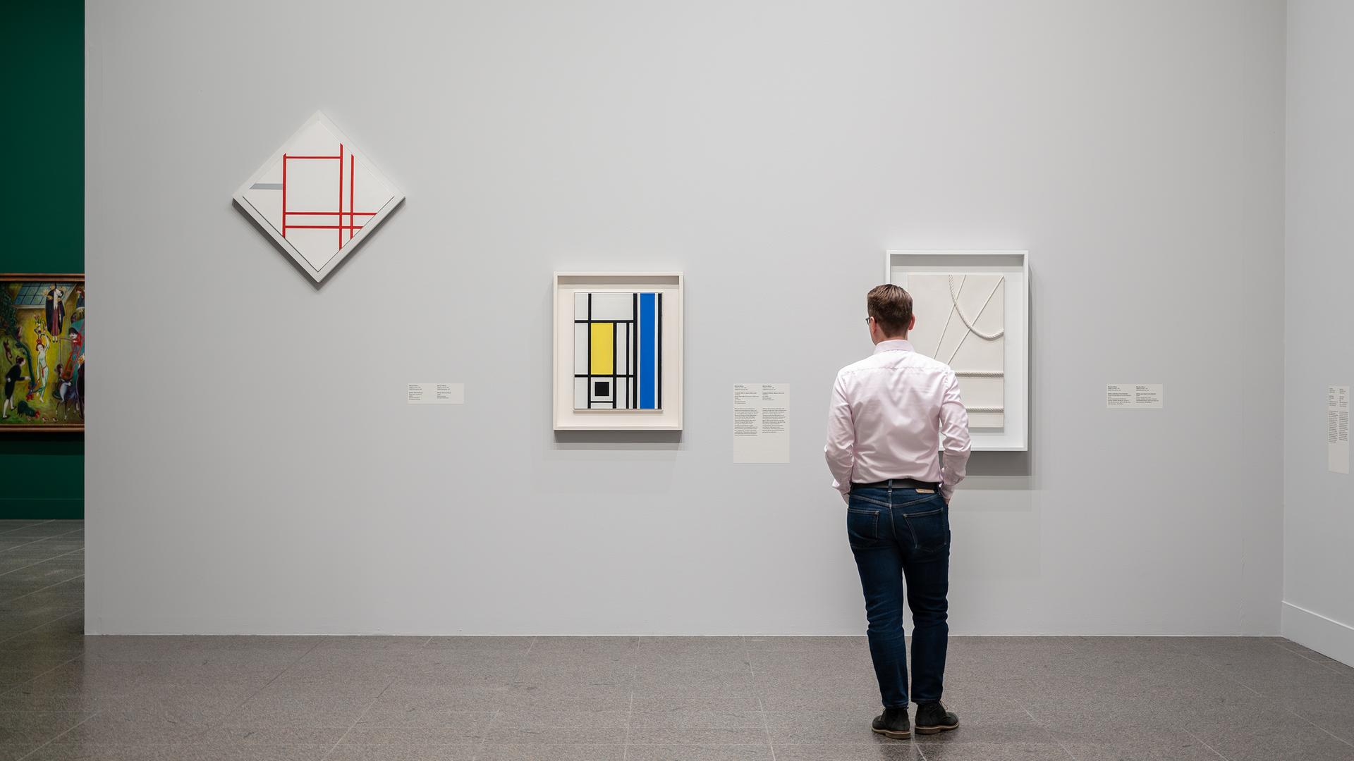 Ein Mann sieht sich moderne Gemälde an, die in einem Ausstellungsraum an der Wand hängen.