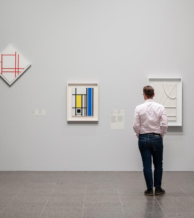 Ein Mann sieht sich moderne Gemälde an, die in einem Ausstellungsraum an der Wand hängen.