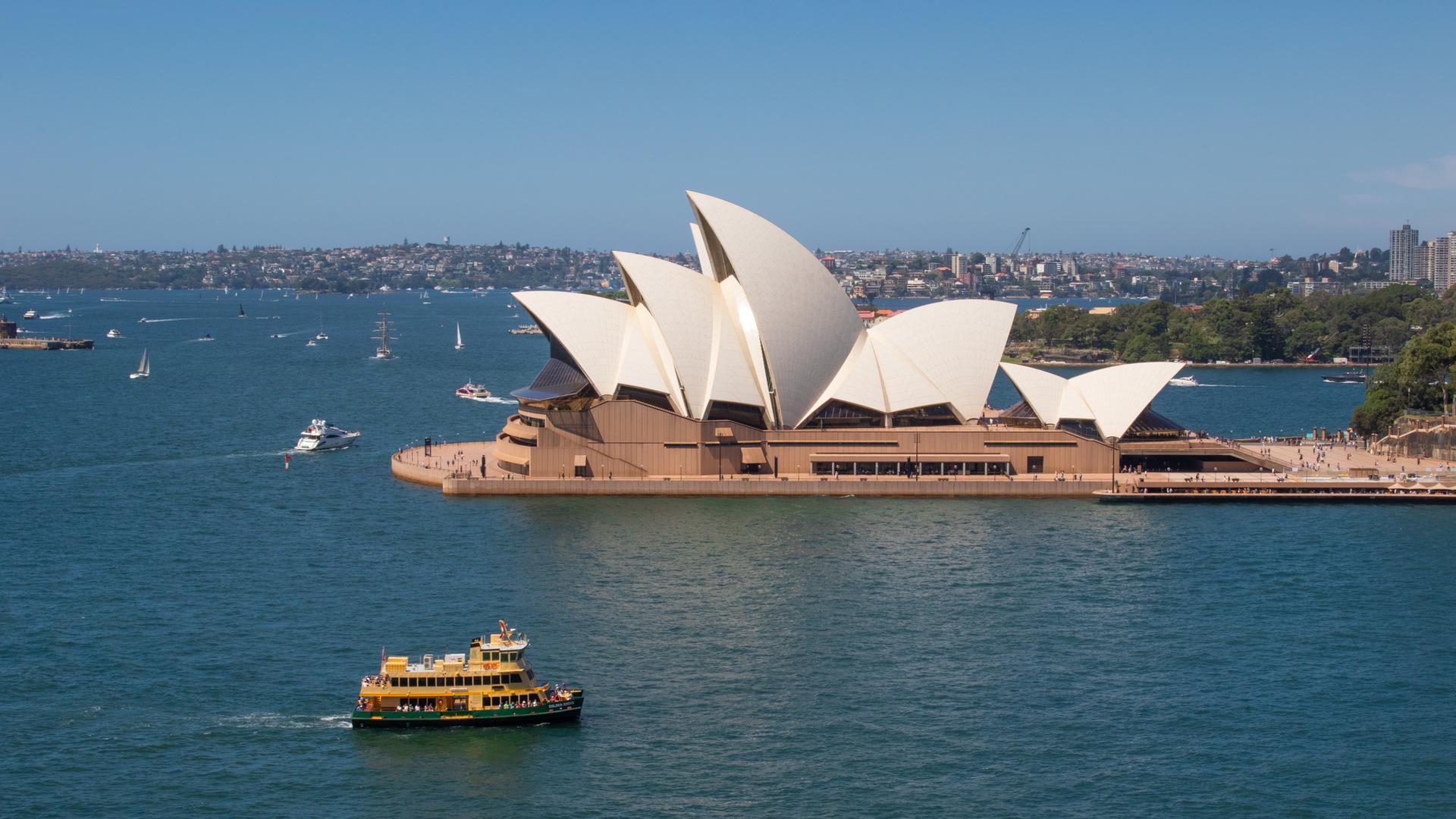 Panoramabild des Opernhauses von Sydney. Auf dem Wasser rund um das Gebäude sind mehrere Boote zu erkennen.