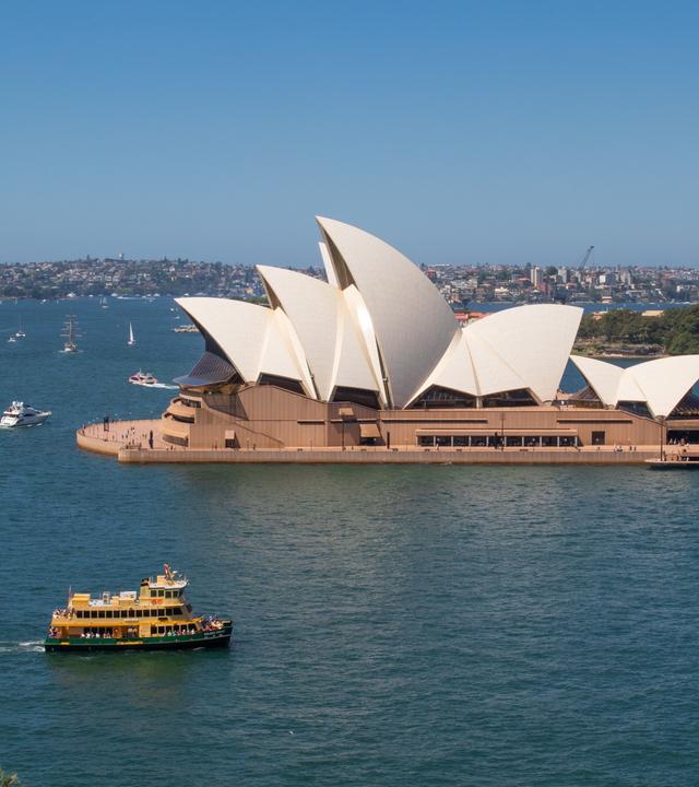 Panoramabild des Opernhauses von Sydney. Auf dem Wasser rund um das Gebäude sind mehrere Boote zu erkennen.