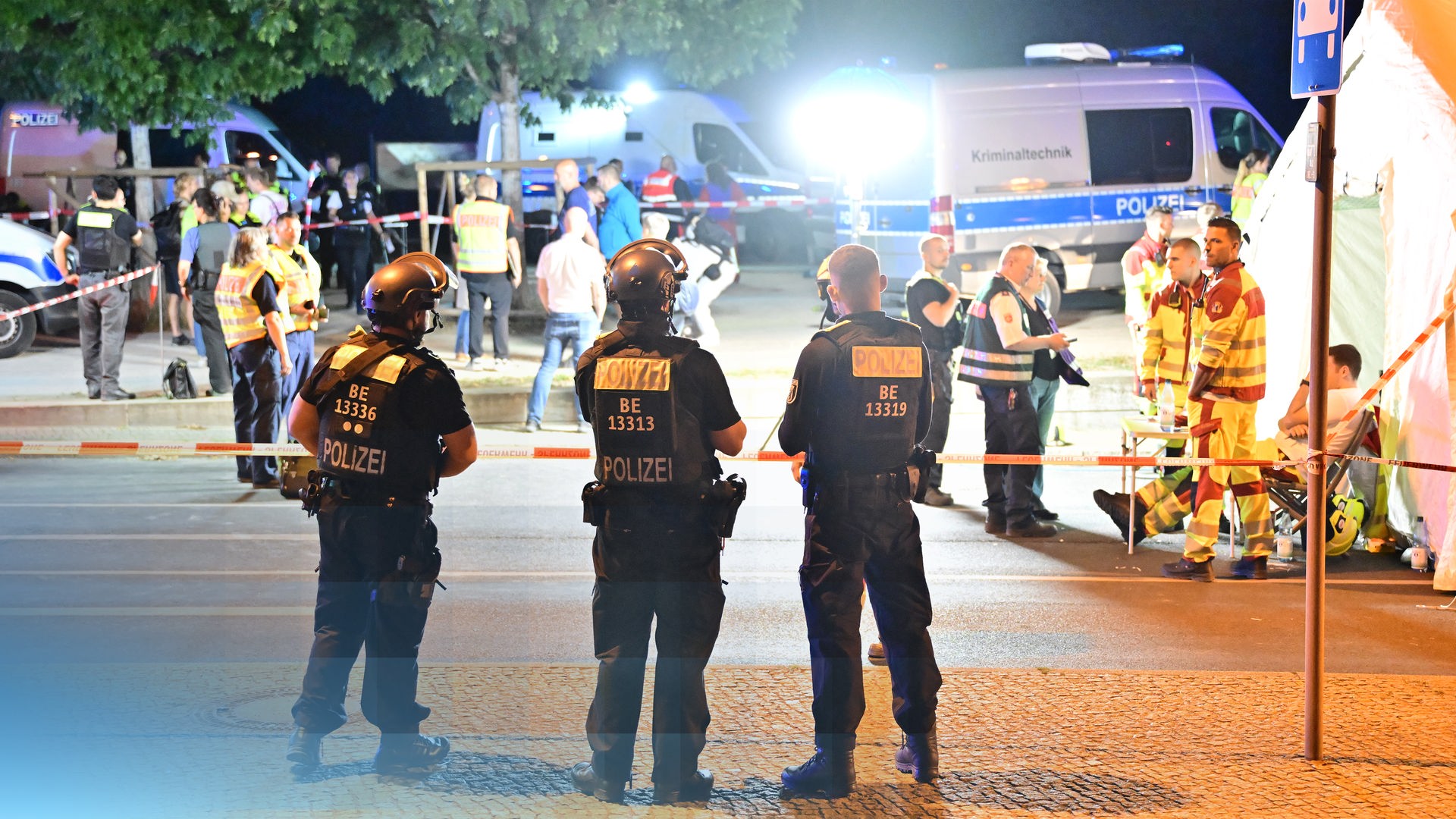 Drei Polizisten stehen am Einsatzort. Im Hintergrund stehen andere Rettungskräfte und Einsatzfahrzeuge