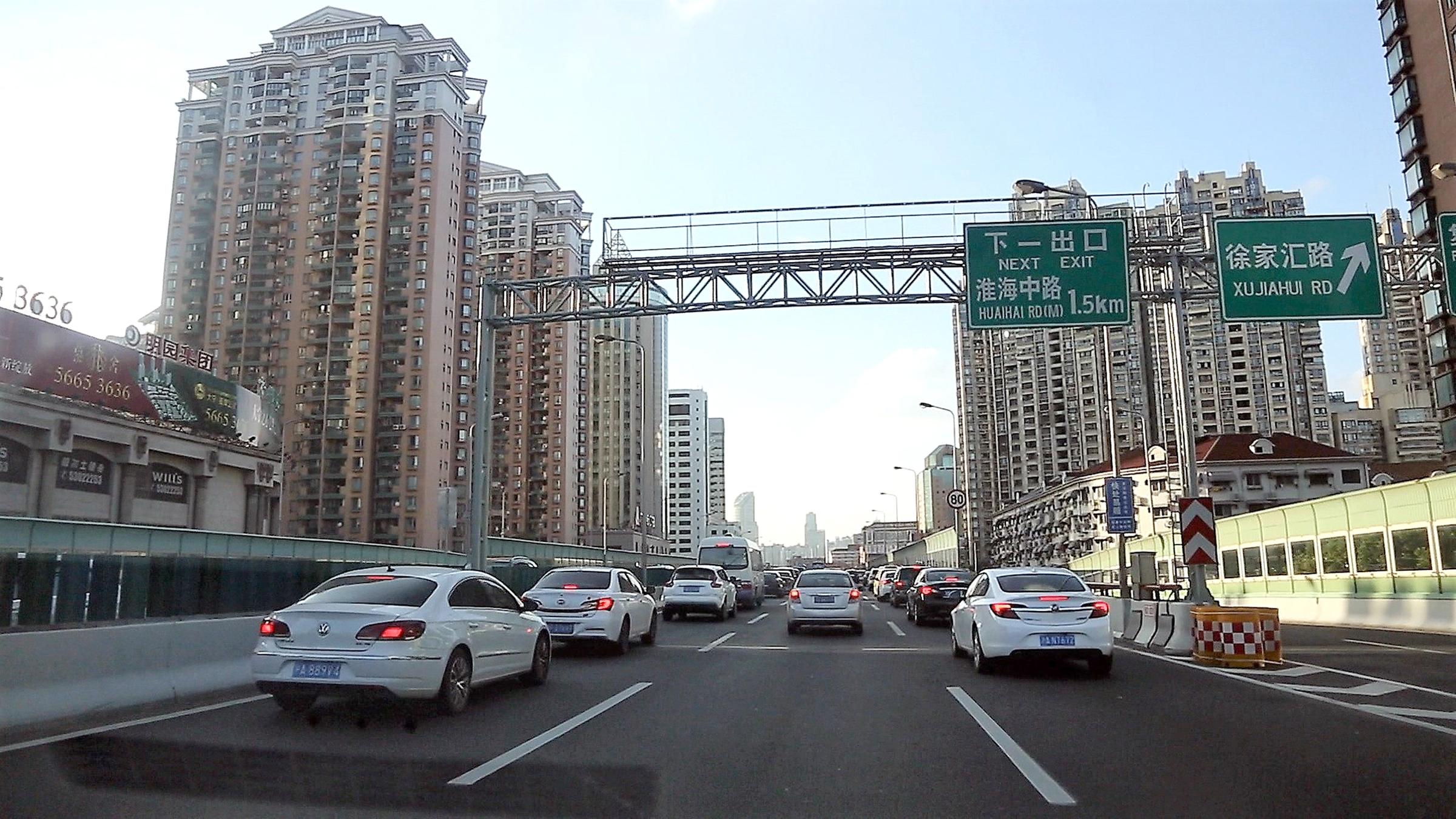 Blick auf eine dreispurige Straße entlang von Häuserschluchten, auf der Autos entlangfahren.