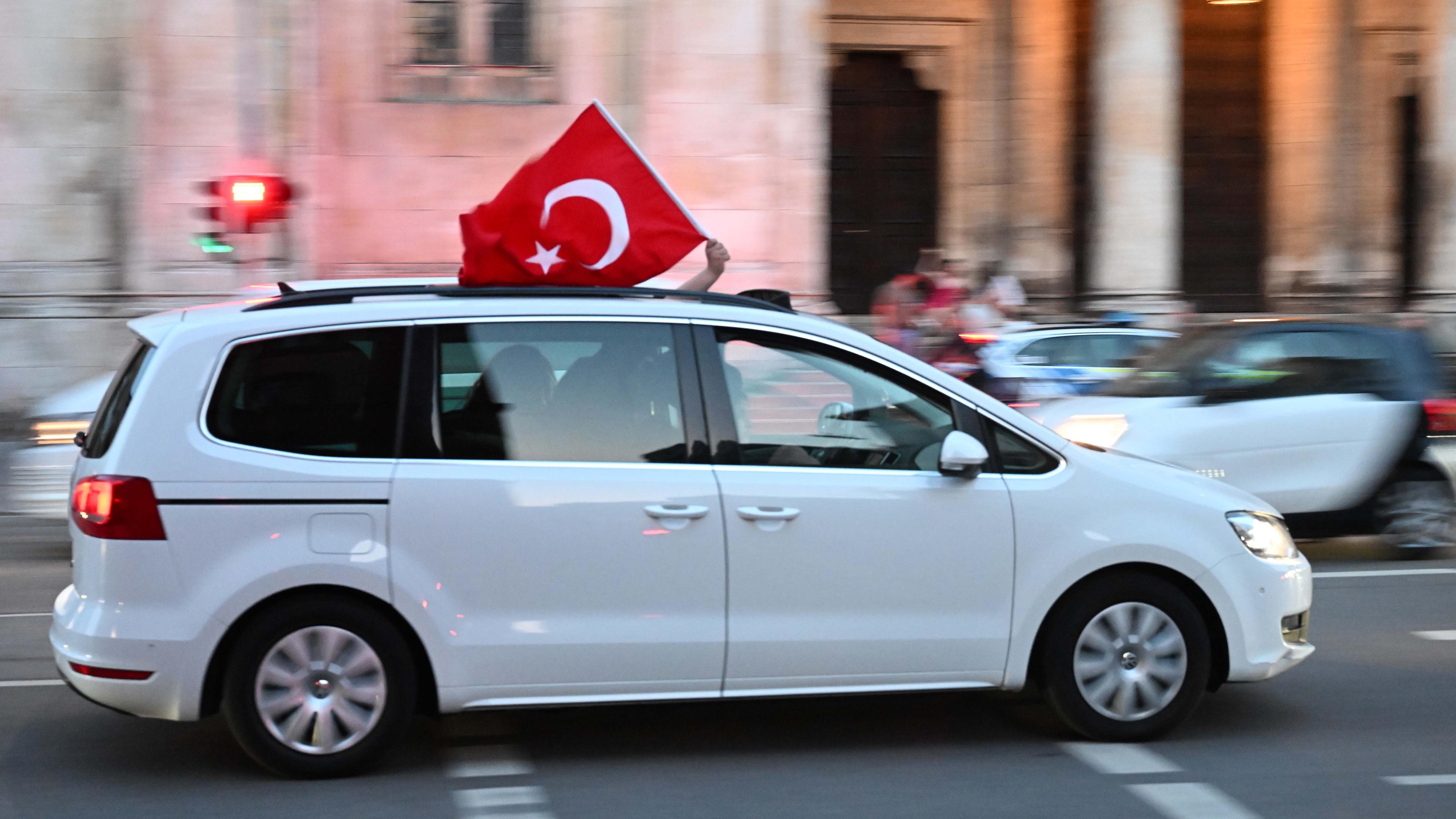 Aus einem fahrenden weißen Auto wird eine türkische Flagge gehalten. 