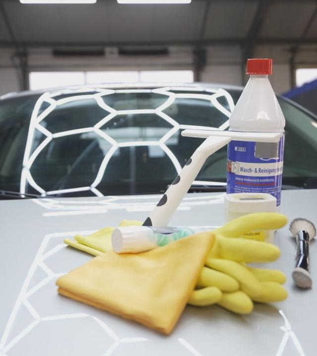 Auto auf dessen Motorhaube verschiedene Reinigungs-Gegenstände liegen