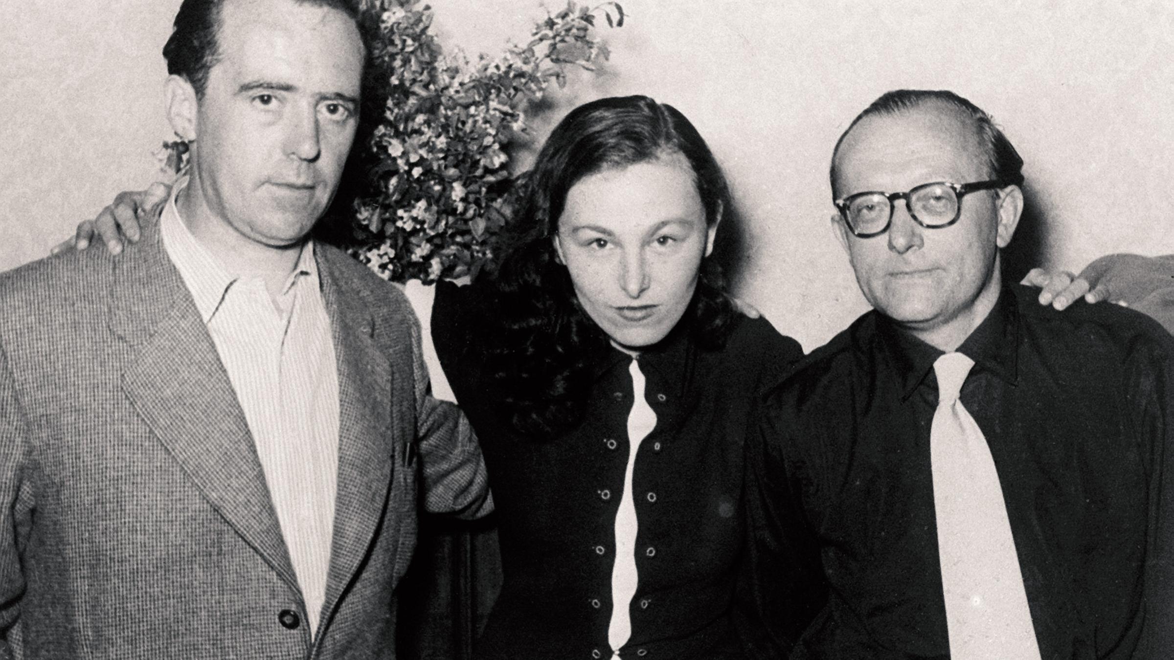 Schwarz-weiß-Foto von zwei Männern und einer Frau, die zwischen den beiden steht.