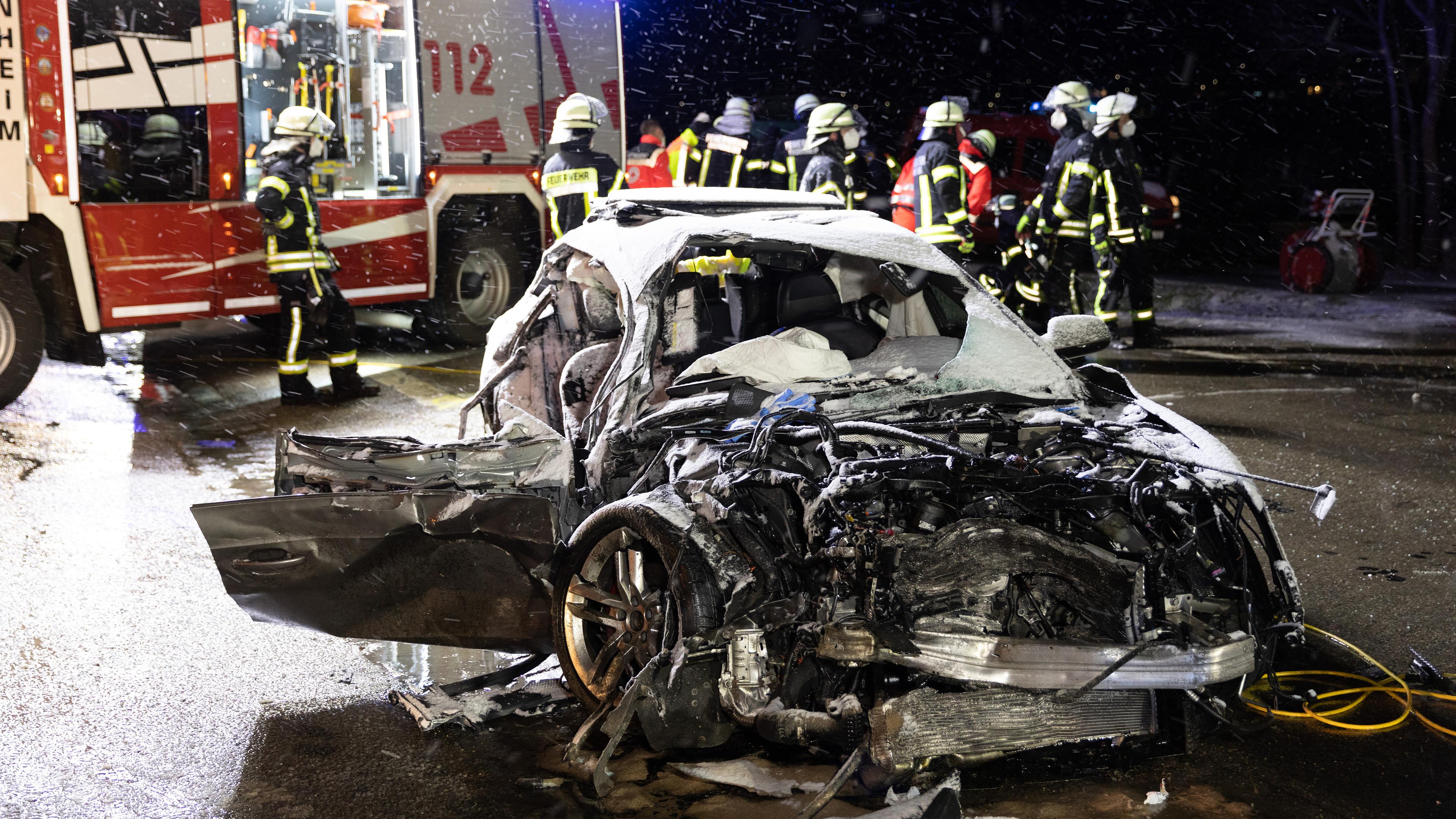 Feuerwehrleute stehen an einer Unfallstelle hinter einem Autowrack, aufgenommen am 06.04.2021 in Monheim