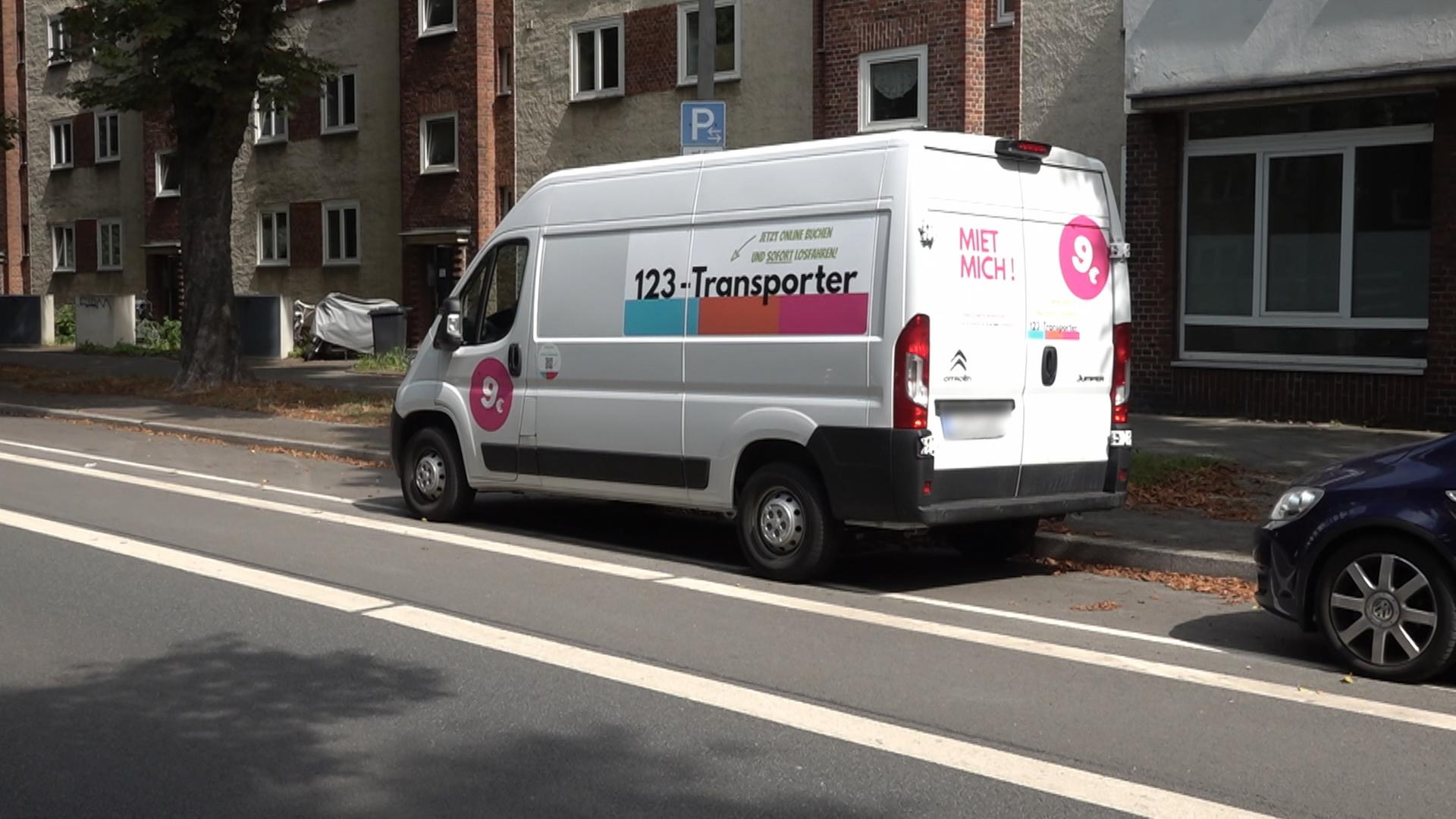 Ein 123-Transporter steht am Straßenrand vor einem Mietshaus 