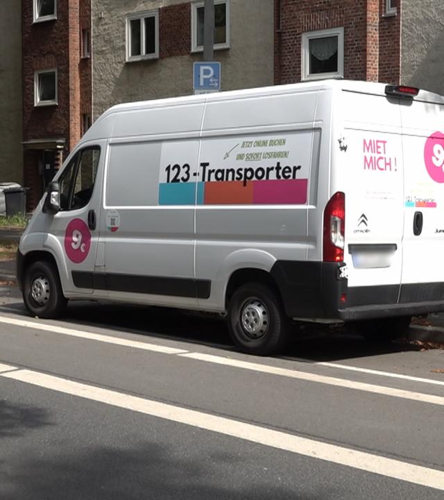 Ein 123-Transporter steht am Straßenrand vor einem Mietshaus 