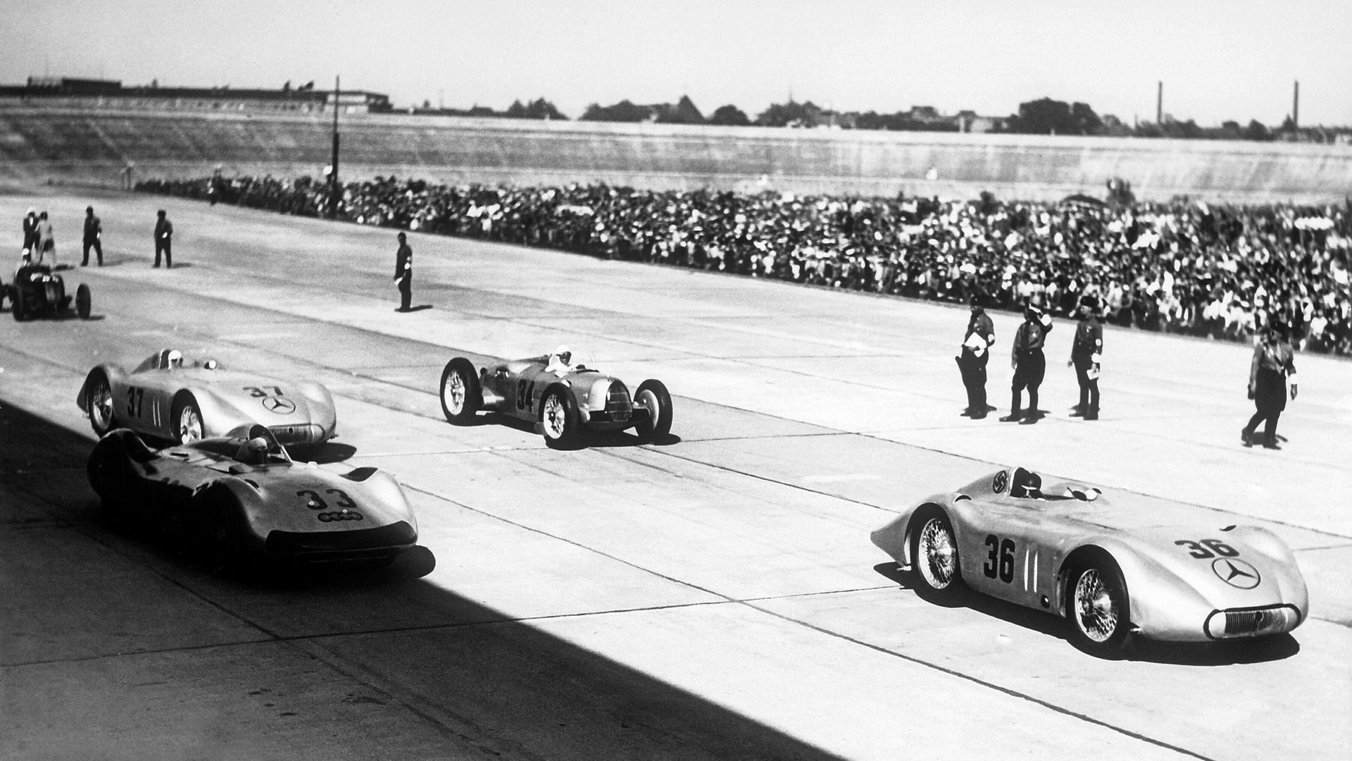 Ein Schwarz-Weiß-Bild von sechs alten Rennwagen. Im Vordergrund ist ein Mercedes mit der Nummer 36 zu sehen.
