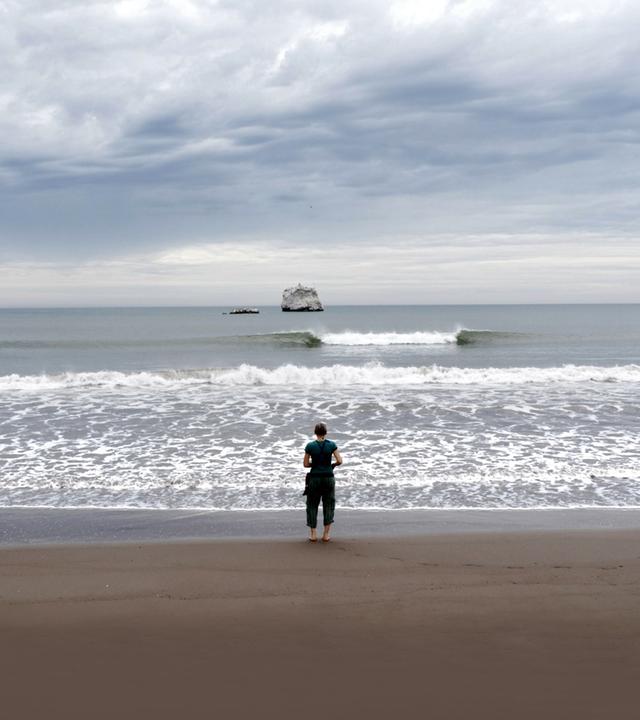 Frau mit dem Rücken zur Kamera am Strand vor Meer.