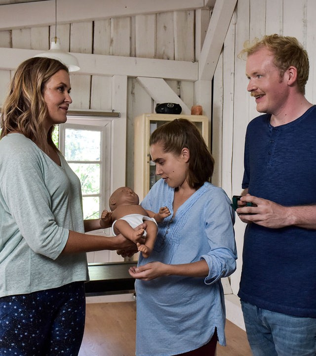 "Lena Lorenz - Baby auf Probe": In der Hebammenpraxis überreicht Lena Lorenz (Judith Hoersch) der schwangeren Alina Moosleitner (Anne-Marie Lux) eine Babypuppe. Daneben steht Tim Scheuer (Sebastian Griegel) und schaut freudig.