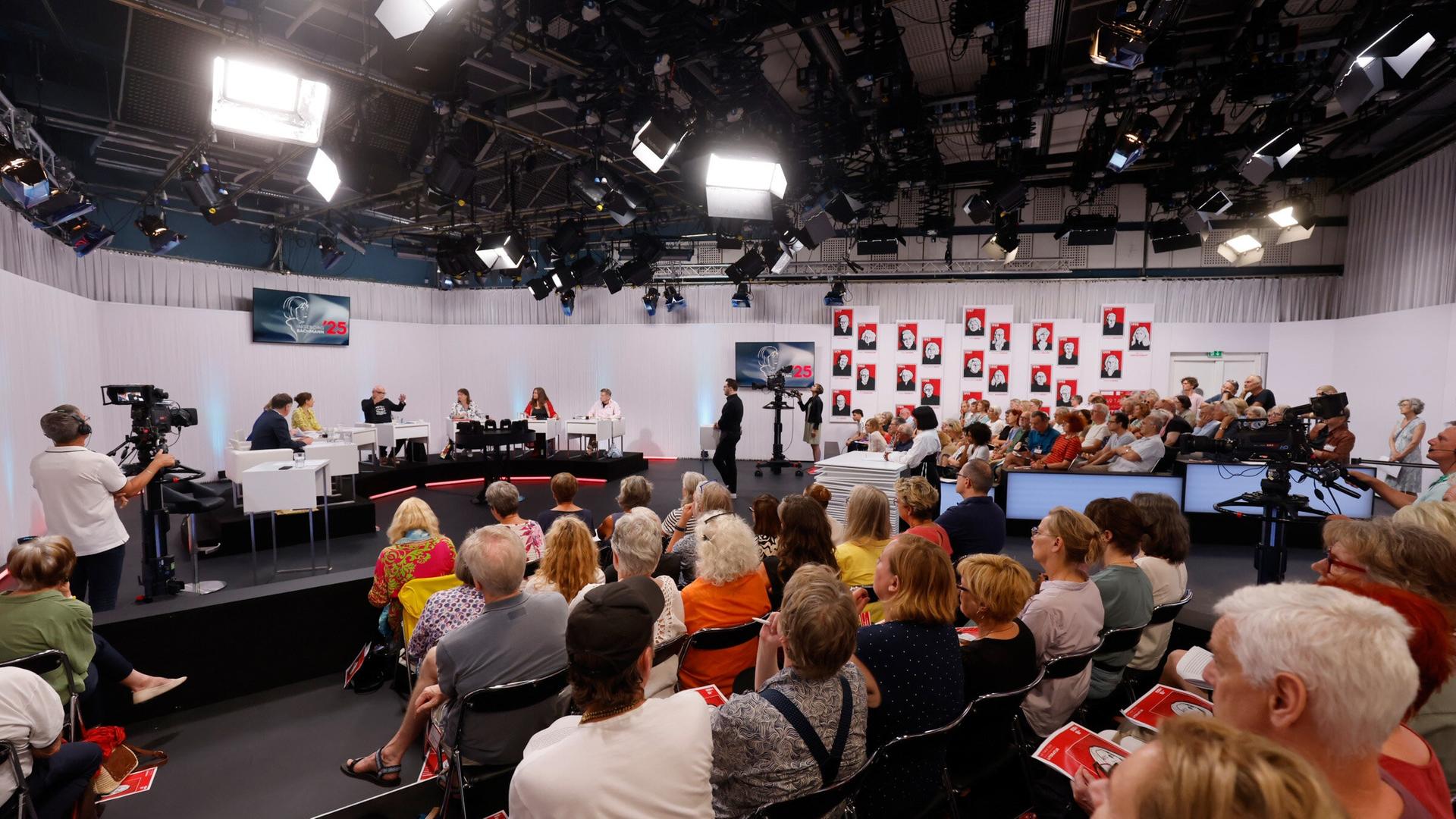 Blick ins vollbesetzte ORF-Studio während einer Jury-Sitzung der Tage der deutschsprachigen Literatur  mit Kamerateams, Publikum und großflächiger Porträtgalerie im Hintergrund.