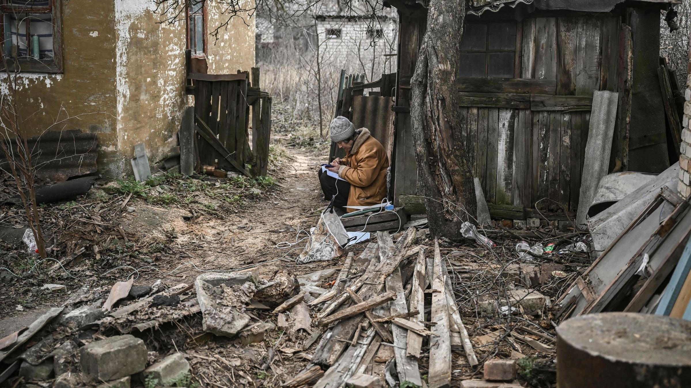 Eine Frau macht sich Notizen und benutzt ihr Smartphone, während sie am 24. 3. 2023 in der Nähe von Bachmut auf dem Hof eines Hauses sitzt.