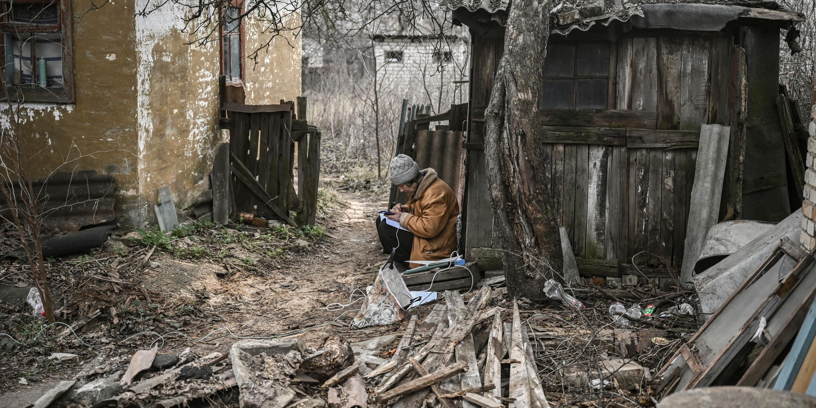 Eine Frau macht sich Notizen und benutzt ihr Smartphone, während sie am 24. 3. 2023 in der Nähe von Bachmut auf dem Hof eines Hauses sitzt.