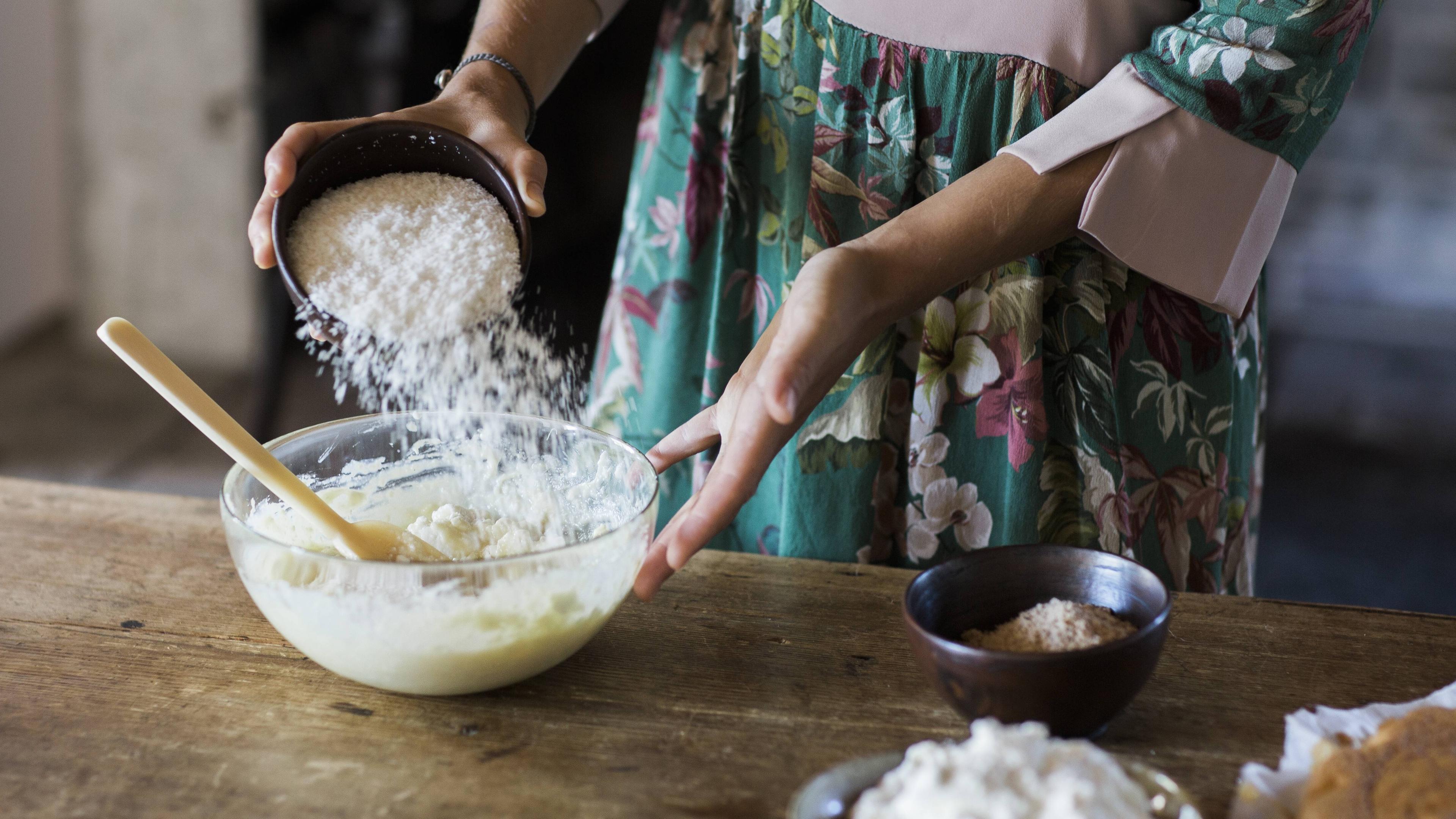 Eine Frau bereitet einen Kuchenteig zu, indem sie Mehl in eine Schüssel gibt.