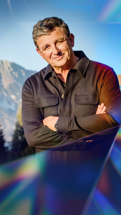 Schauspieler Hans Sigl steht vor einem Bergpanorama.