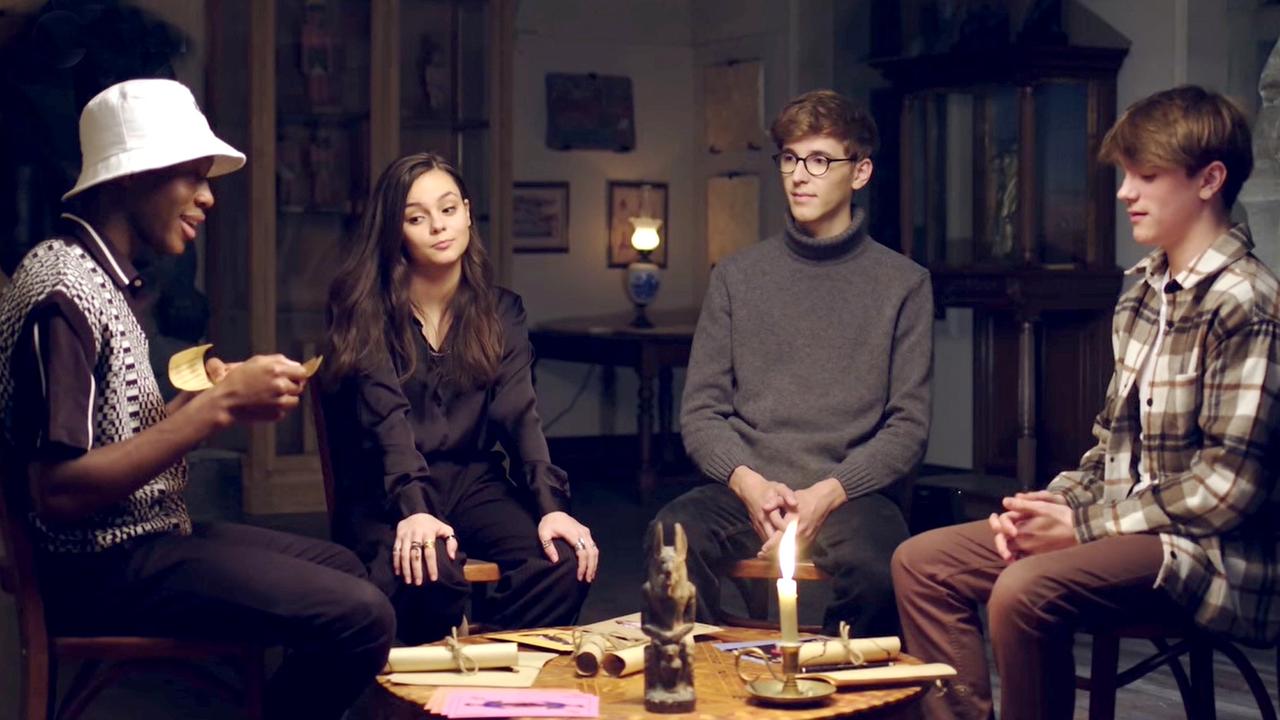 Nana, Eloise, ein Spielleiter und Frankie spielen ein Escape Game am Tisch bei Kerzenschein.