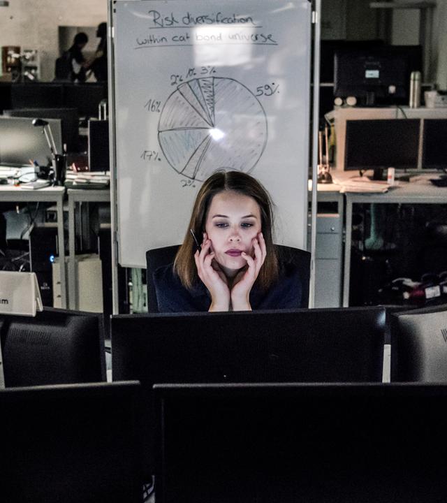 Jana Liekam (Paula Beer) sitzt an ihrem Schreibtisch hinter mehreren Bildschirmen und arbeitet. Im Hintergrund sind ein Chartboard und viele Computer zu sehen.