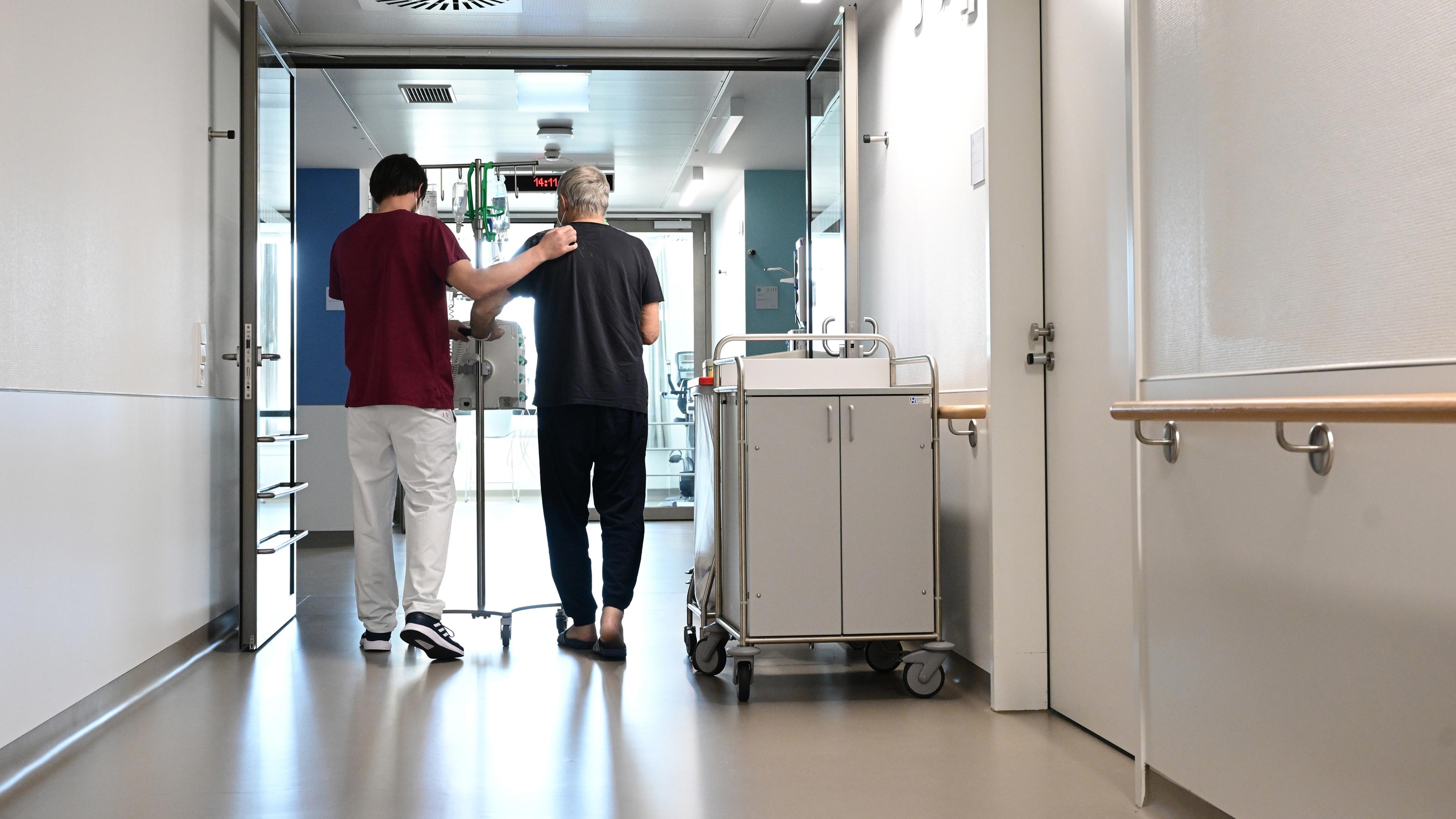 Baden-Württemberg, Stuttgart: Ein Pfleger geht im Klinikum Stuttgart mit einem Patienten über einen Flur.