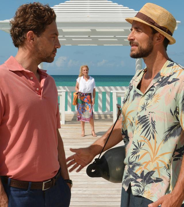  Auf einem Anlegesteg stehen sich Toby Heers (Max Alberti) und Philip Singer (Leander Lichti) gegenüber und reden miteinander. Im Hintergrund steht Melanie Singer (Aline Hochscheid) und beobachtet die beiden.