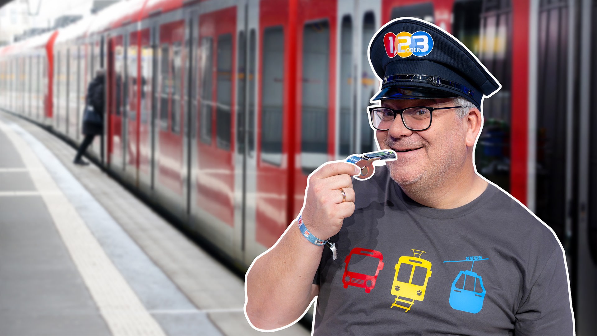 Elton steht mit Trillerpfeife in der Hand und einer Lokführermütze vor einem Zug. 