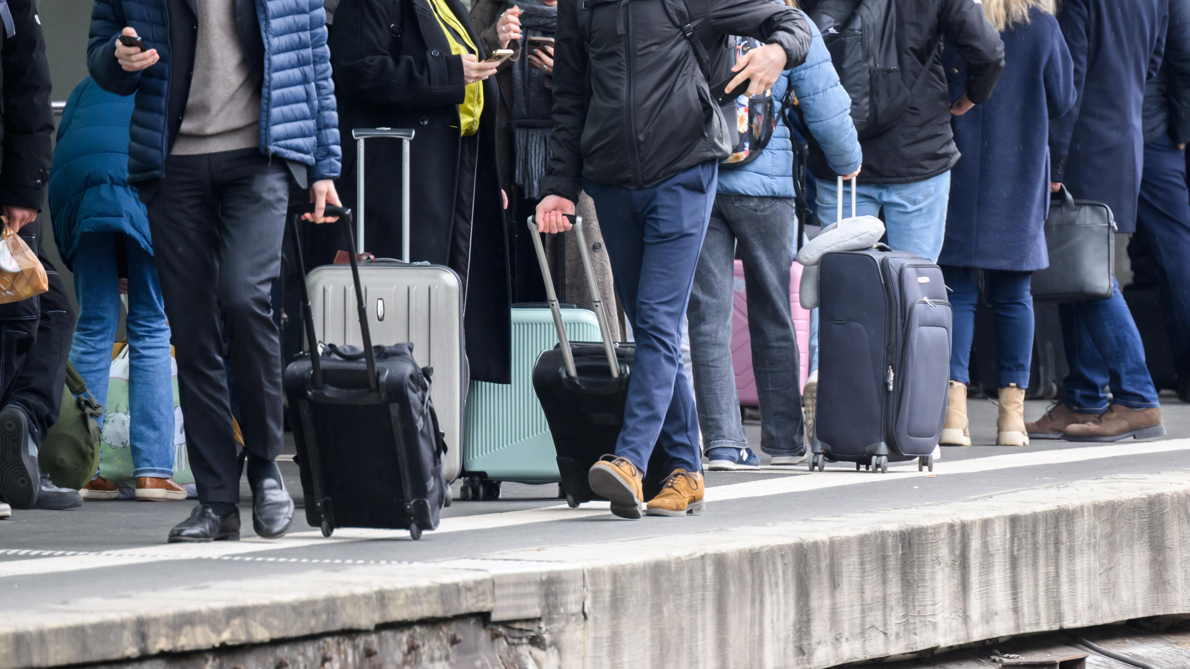 Reisende stehen mit Taschen und Koffern an einem Gleis im Hauptbahnhof Hannover.